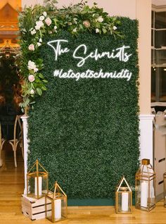 a green wall with white flowers and greenery on it, surrounded by candles in front of the sign