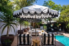 an outdoor patio with black and white striped chairs, umbrella and pool in the background