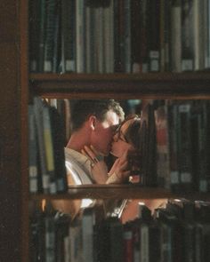 a man and woman kissing in front of a book shelf with many books on it