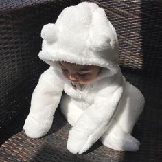 a baby in a white teddy bear costume sitting on a bench and looking at the camera