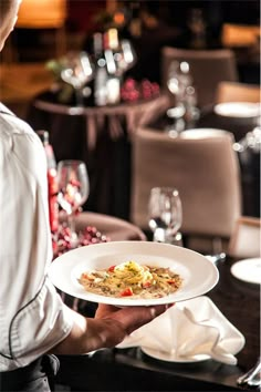 a man holding a plate with food on it in front of a table full of wine glasses