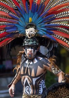 a man in an elaborate headdress walks down the street with feathers on his head