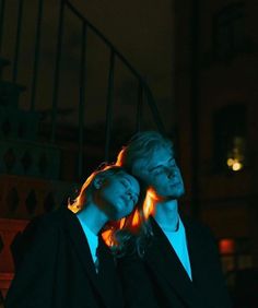 a man and woman sitting next to each other in front of a staircase at night