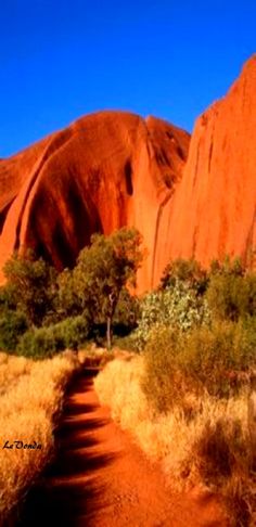 a dirt path in front of a large rock formation