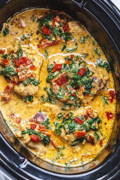 a crock pot filled with chicken, spinach and tomato sauce in the slow cooker