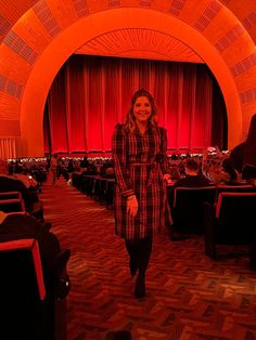 a woman standing in front of a red curtain at an auditorium with rows of seats