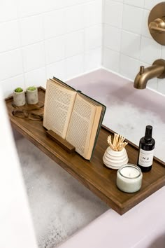 an open book sitting on top of a wooden tray in a bathtub with soap and toothbrushes