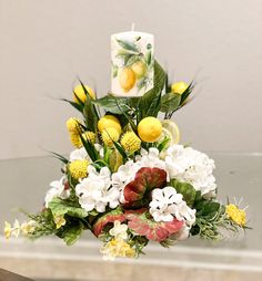 a vase filled with yellow and white flowers next to a lit candle on top of a table