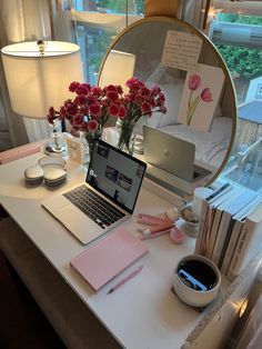 a laptop computer sitting on top of a white desk next to a vase with flowers