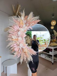 a woman standing in front of a mirror holding a pink and white feathered object