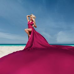 a woman in a pink dress is posing on the beach with her arms behind her head