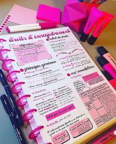 a pink notebook with writing on it next to some pens and sticky notes in spanish