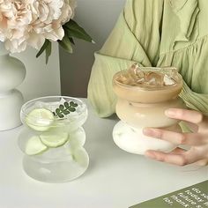 a woman is holding a glass with some liquid in it next to other vases and flowers