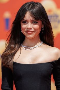 a woman with long hair wearing a black dress and diamond necklace smiling at the camera