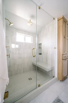 a bathroom with a walk in shower next to a white sink and wooden cabinetry