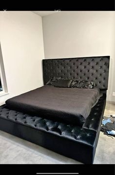 a large bed with black leather headboard and foot board in a white walled room