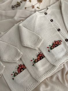 four white sweaters with flowers on them are laying on the bed together, and there is no image to describe