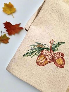 an embroidered pouch with oranges on it next to autumn leaves and acorns