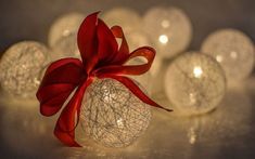 a red bow on top of a white ball ornament with lights in the background