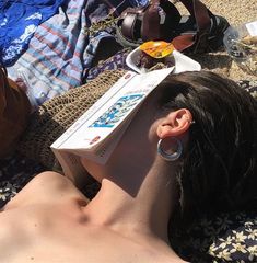 a woman laying on top of a beach next to an open book with ear rings