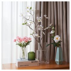 three vases with flowers are sitting on a table next to a book that says more