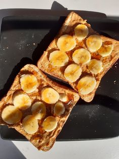 two pieces of toast with bananas and peanut butter on them sitting on a black plate