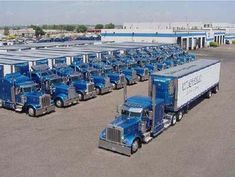 several semi trucks are parked in a parking lot next to each other and one truck is blue