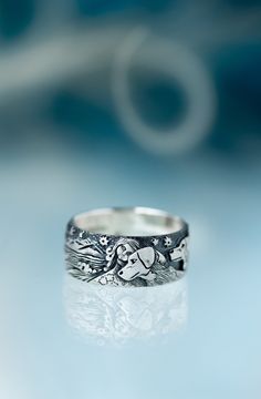 a silver ring sitting on top of a white table next to a blue background with an image of a dog