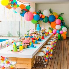 a long table with many colorful balloons and decorations on it, next to a swimming pool