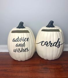 two white pumpkins with words painted on them sitting on a wooden floor next to each other