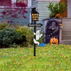 a street sign with ghost and pumpkins on it in front of a house that is decorated for halloween