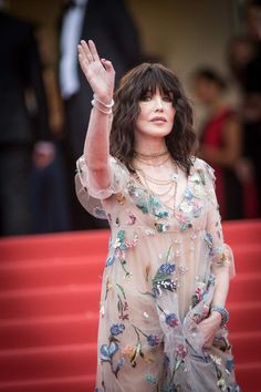 a woman waves to the crowd as she walks down a red carpeted area with her hand in the air