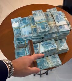 a person is holding money in front of a table full of stacks of bank notes