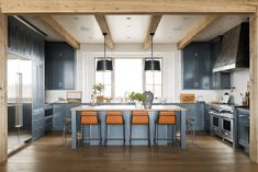 an open kitchen with blue cabinets and orange chairs in the island countertop, along with wooden beams on the ceiling