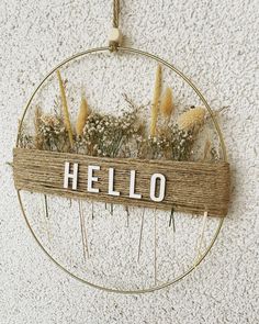 a wooden sign that says hello hanging on the wall next to some dried grass and flowers