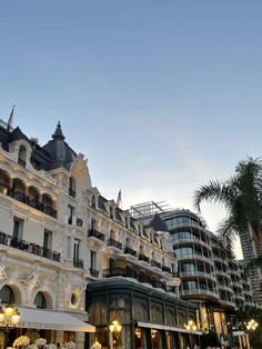 the hotel is lit up at night in front of palm trees and other building with balconies