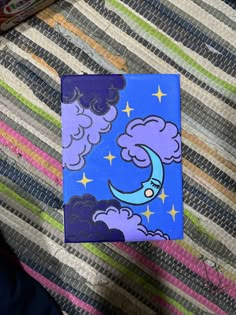 a blue notebook with a cartoon moon and clouds on it sitting on a striped surface