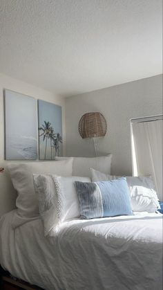 a bed with white linens and pillows in a bedroom next to two pictures on the wall