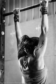 a woman doing pull ups on a bar in a crossfit gym with her hands behind her head