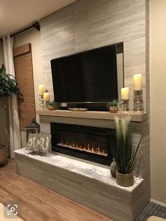 a living room with a fireplace and tv on the wall, surrounded by candles in front of it