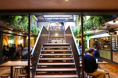 people are sitting at tables and stairs in a restaurant with plants growing on the walls