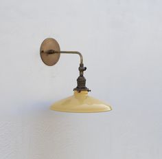 an old fashioned wall mounted light on the side of a white wall with a yellow shade