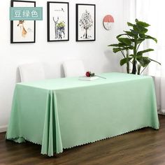 there is a table with a green cloth on it in front of pictures and a potted plant