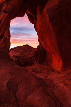 a red rock formation with the sun setting in the background and an opening to another one