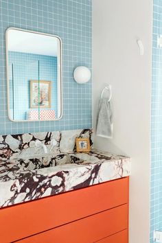 a bathroom with blue tile and orange cabinetry in the sink area, along with a mirror on the wall