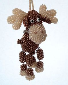 a beaded moose ornament hanging from a string on a white background with reflection