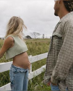 a pregnant woman standing next to a man near a fence