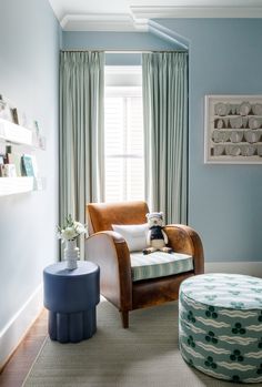 a living room with blue walls and curtains, a chair in the corner and a footstool on the floor