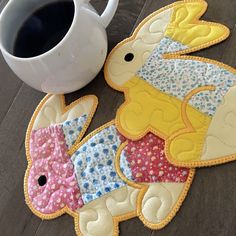 a cup of coffee sitting next to two patchwork elephant coasters on top of a wooden floor