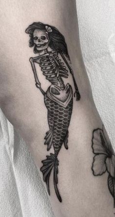 a skeleton tattoo on the arm of a woman with a flower in her left hand